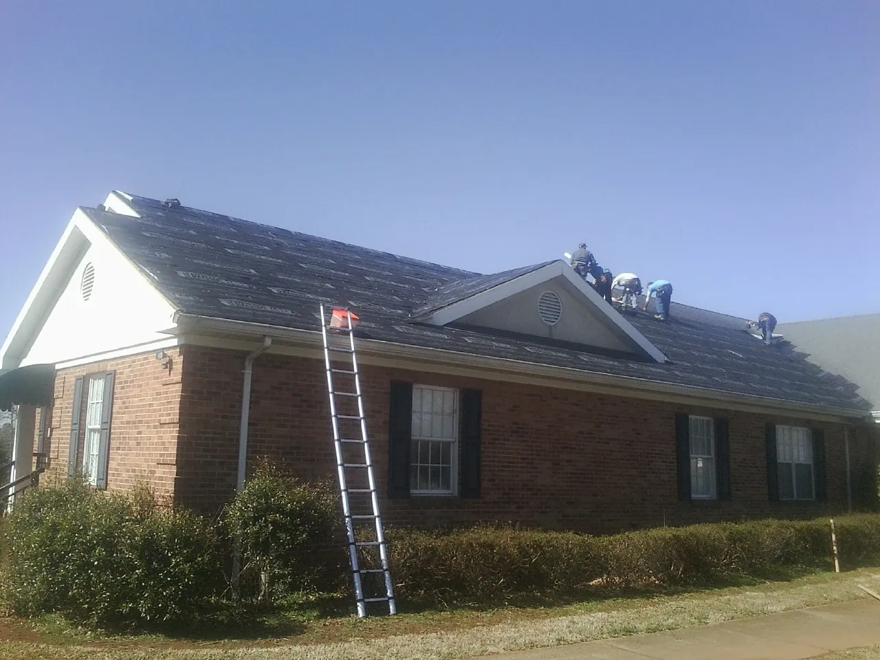Crew tearing shingles off a brick ranch roof with a ladder set — Metal Roof Repair work by our crew in Mendham