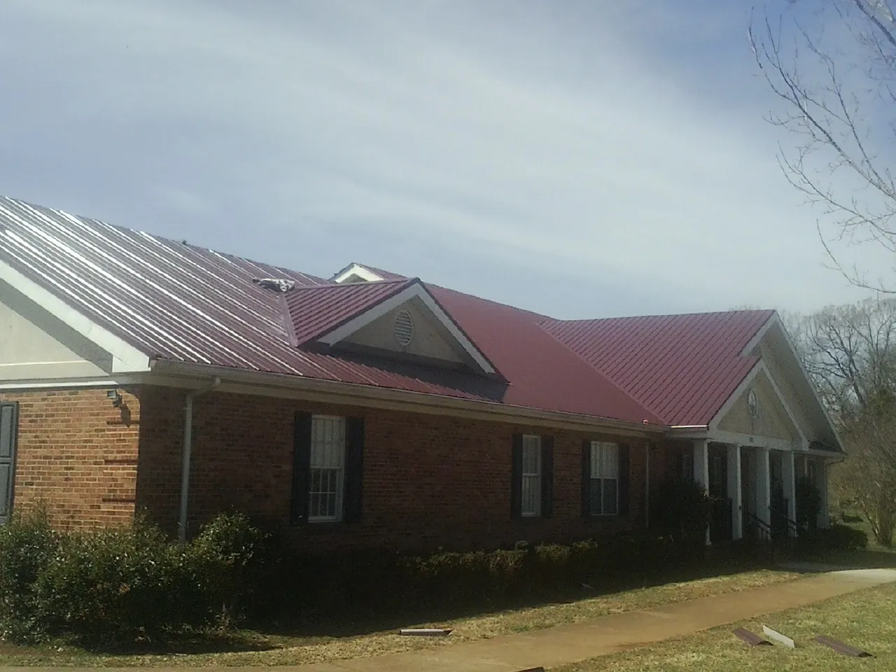 Red metal roof with gabled entries on a long brick building, from a Hail Damage Roof Repair job in Mendham