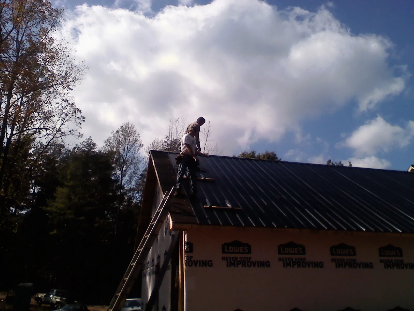 Roofer fastening dark metal panels high against a cloudy sky, from a Roof Inspection job in Mendham
